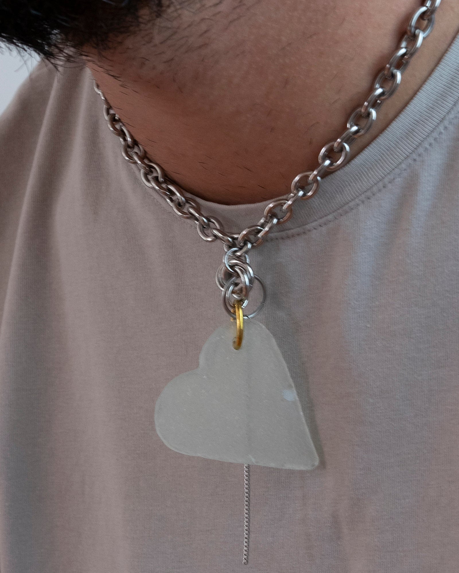 Collier en acier inoxydable. Il s'agit d'un collier ras de cou composé d'une chaine argenté et d'un morceau de verre poli ramassé sur la plage et façonné en forme de coeur.