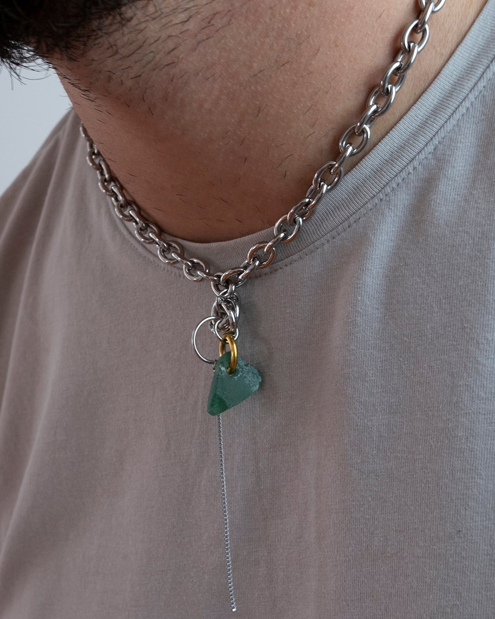 Collier en acier inoxydable. Il s'agit d'un collier ras de cou composé d'une chaine argenté et d'un morceau de verre poli ramassé sur la plage et façonné en forme de coeur.