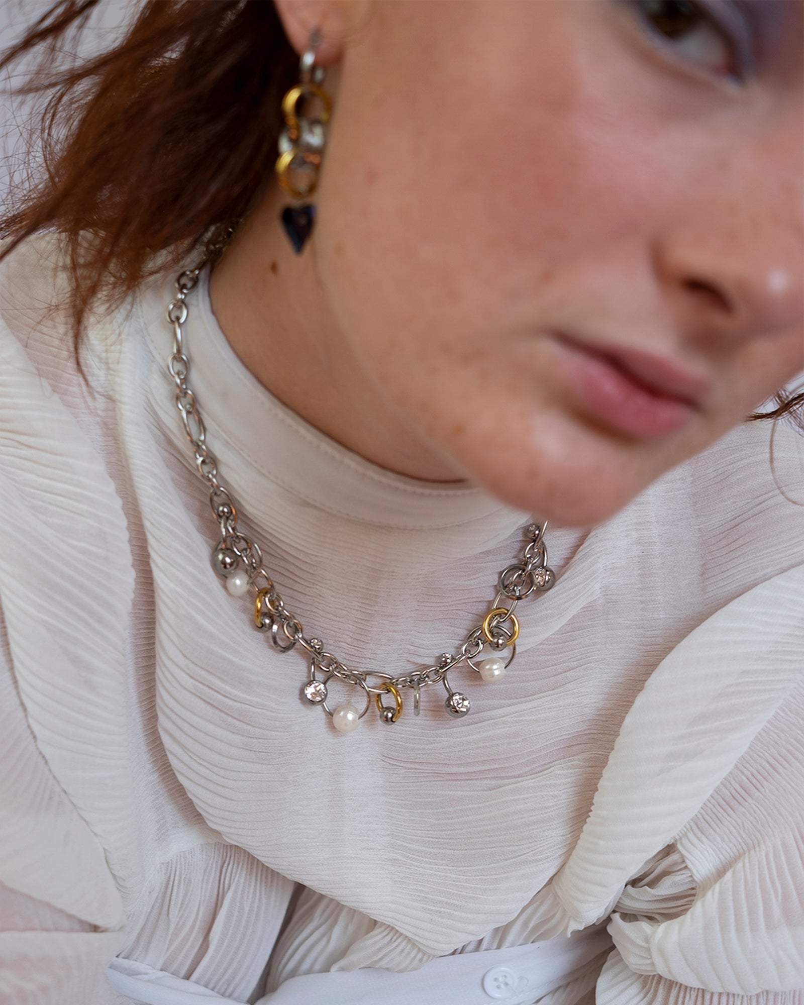 Collier en acier inoxydable. Il s'agit d'un collier composé d'une chaine argenté agrémenté d'anneaux de différentes tailles, de perles de culture d'eau douce ainsi que de piercing