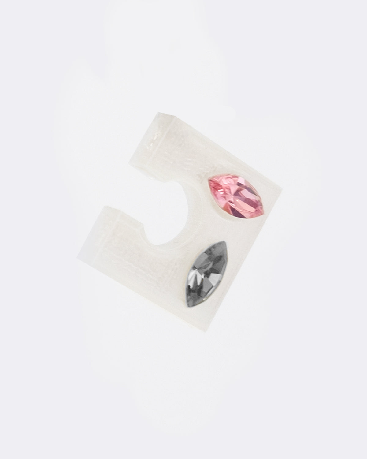 Earcuff en plastique biosourcé. Il s’agit d’un faux piercing pour oreille non perçée qui se positionne au niveau du conch ou du lobe suivant la largeur de l’oreille. Il est composé de deux cristaux rose et gris sur une base transparente carré