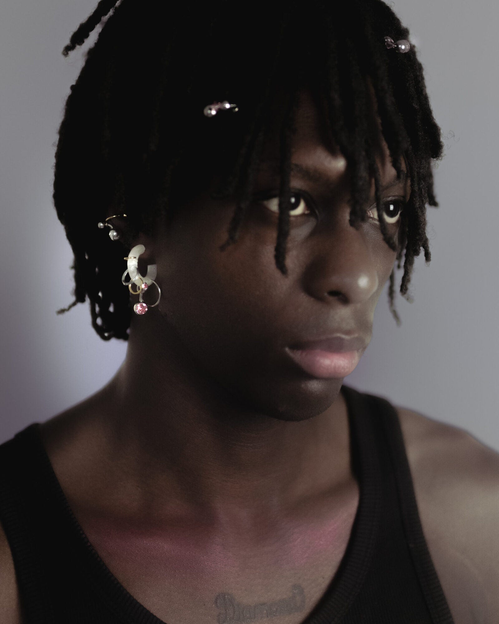 Mono boucle d’oreilles en plastique biosourcé. Elle est composée de différents anneaux dorés et argentés avec un piercing rose sur une base transparente