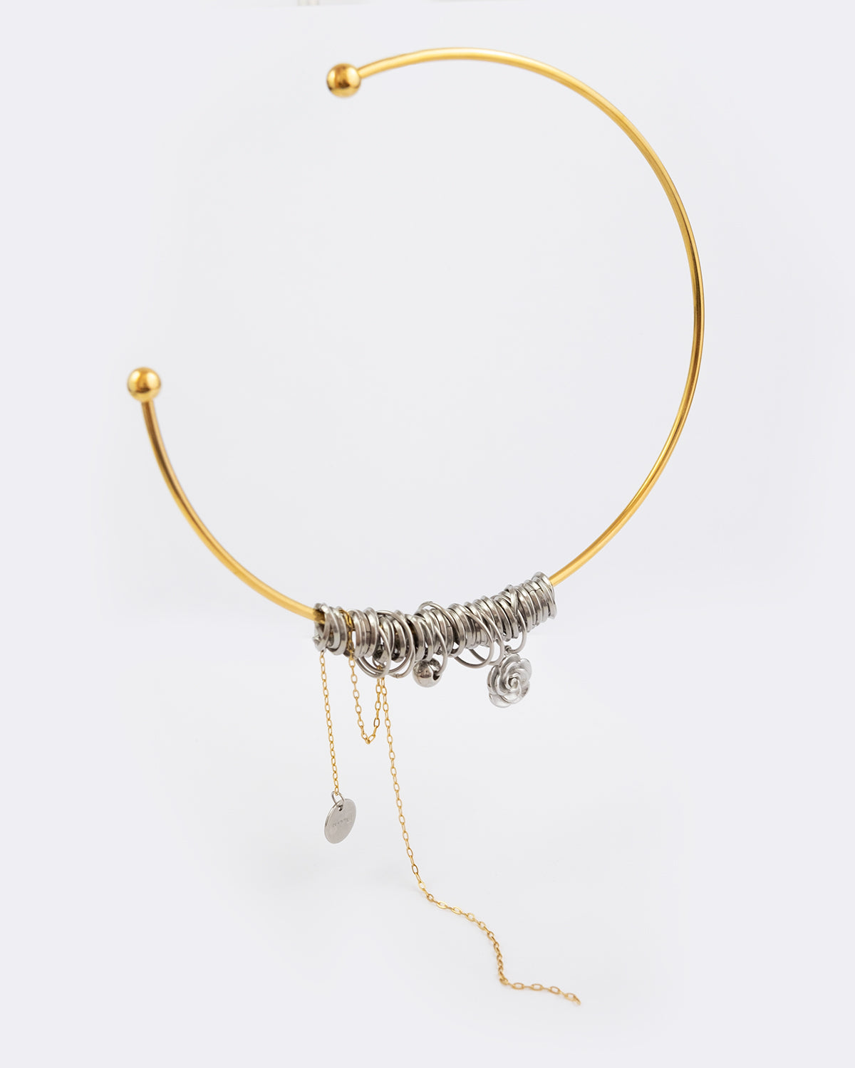 Collier en acier inoxydable. Il s'agit d'un collier composé d'un jonc doré et d'une multitude d'anneaux argentés entremêlés et chaine dorée pendante