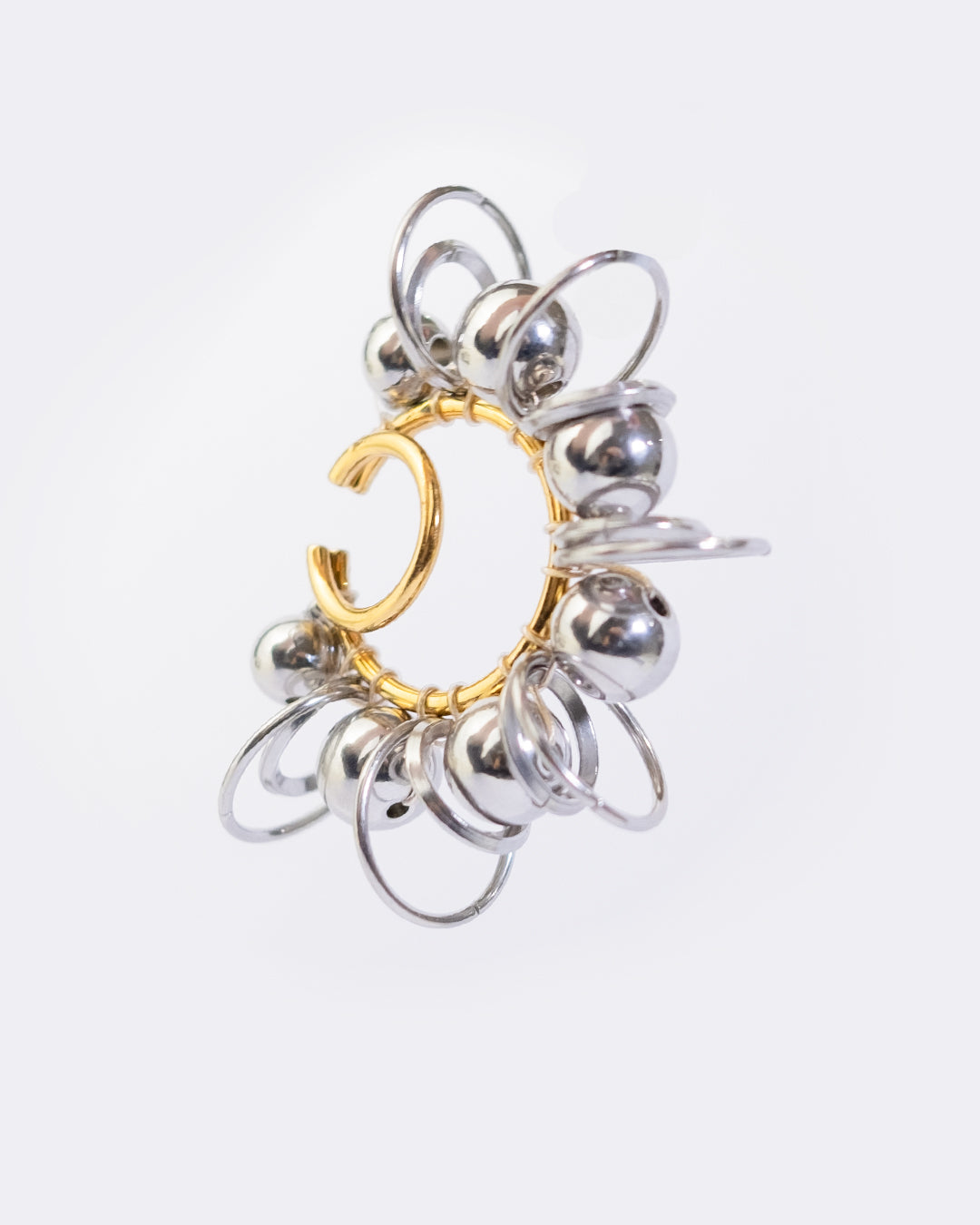 Earcuff en acier inoxydable. Il s’agit d’un faux piercing pour oreille non perçée qui se positionne au niveau du conch ou du lobe suivant la largeur de l’oreille. Il est composé d’un double anneau doré autour duquel sont tressés des perles et anneaux argentés de différentes tailles.