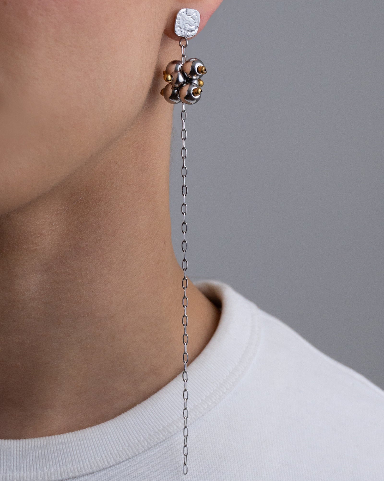 Mono boucle d’oreilles en acier inoxydable composée d’une puce d'oreilles argentée, d'une longue chaine argentée et d’une grappe de perles argentées et dorées dessus.