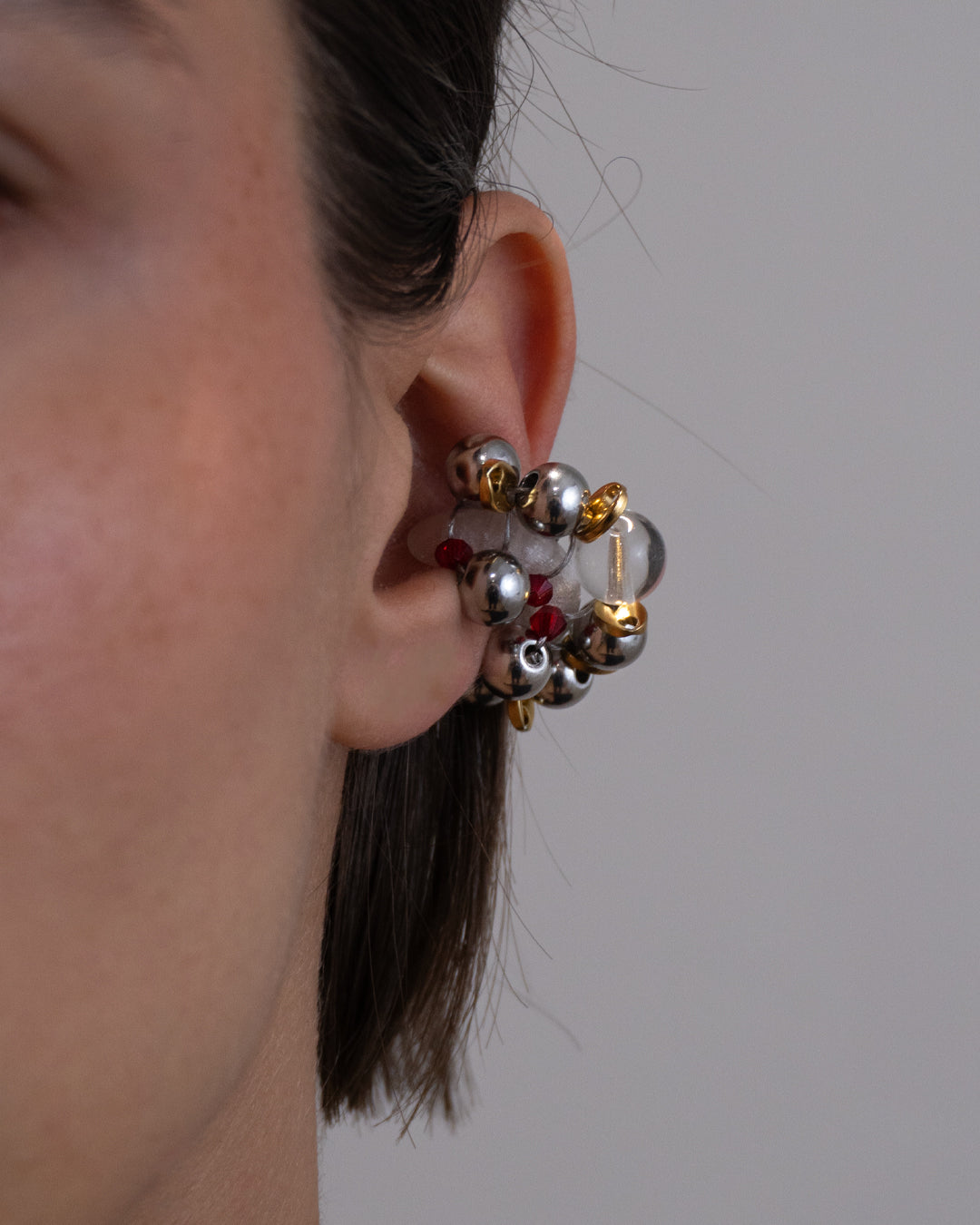 Earcuff Jelly Duo Rouge porté en plastique biosourcé composé d'une multitude de perles argentées de grains de café dorés et de perles en verre colorées rouges tressés sur une base transparente