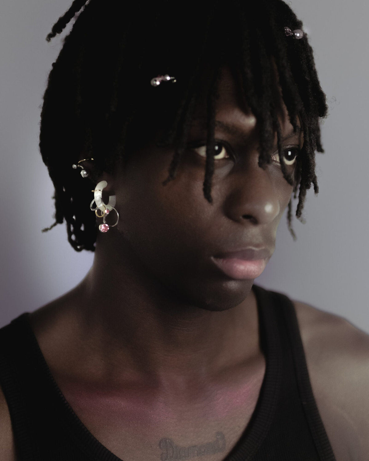 Mono boucle d’oreilles en plastique biosourcé porté composée de différents anneaux dorés et argentés avec un piercing rose sur une base