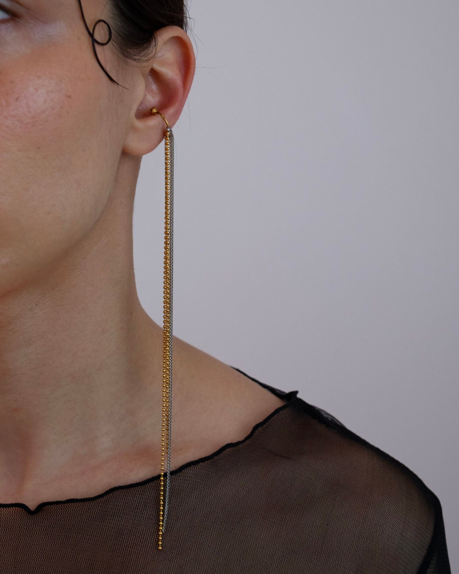 Earcuff en acier inoxydable. Il s'agit d'un faux piercing pour oreille non perçée qui se positionne au niveau du conch ou du lobe suivant la largeur de l'oreille. Il est composé d'un anneau doré et d'une multitude de chaines doré et argenté de différentes longueurs