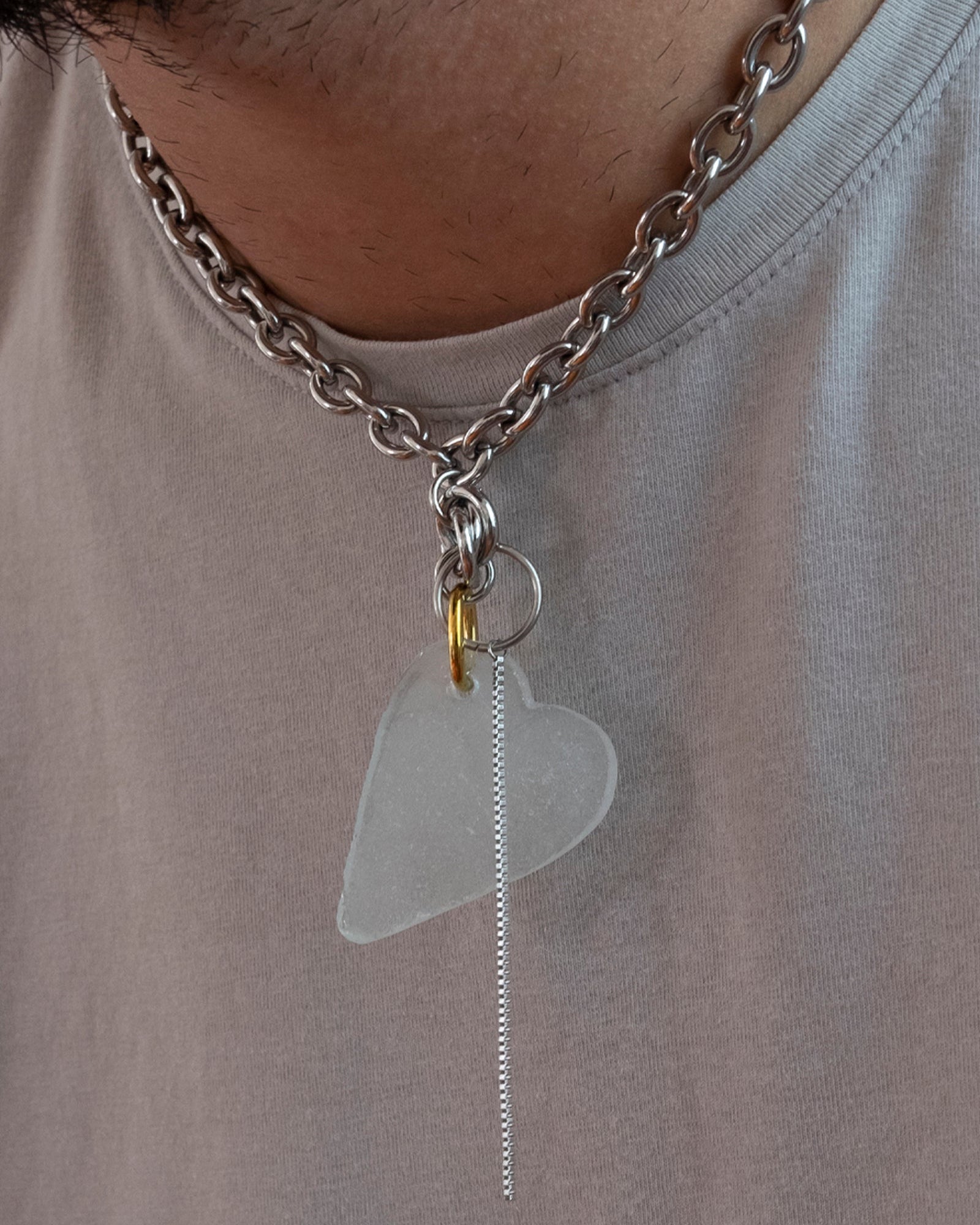 Collier en acier inoxydable. Il s'agit d'un collier ras de cou composé d'une chaine argenté et d'un morceau de verre poli ramassé sur la plage et façonné en forme de coeur.