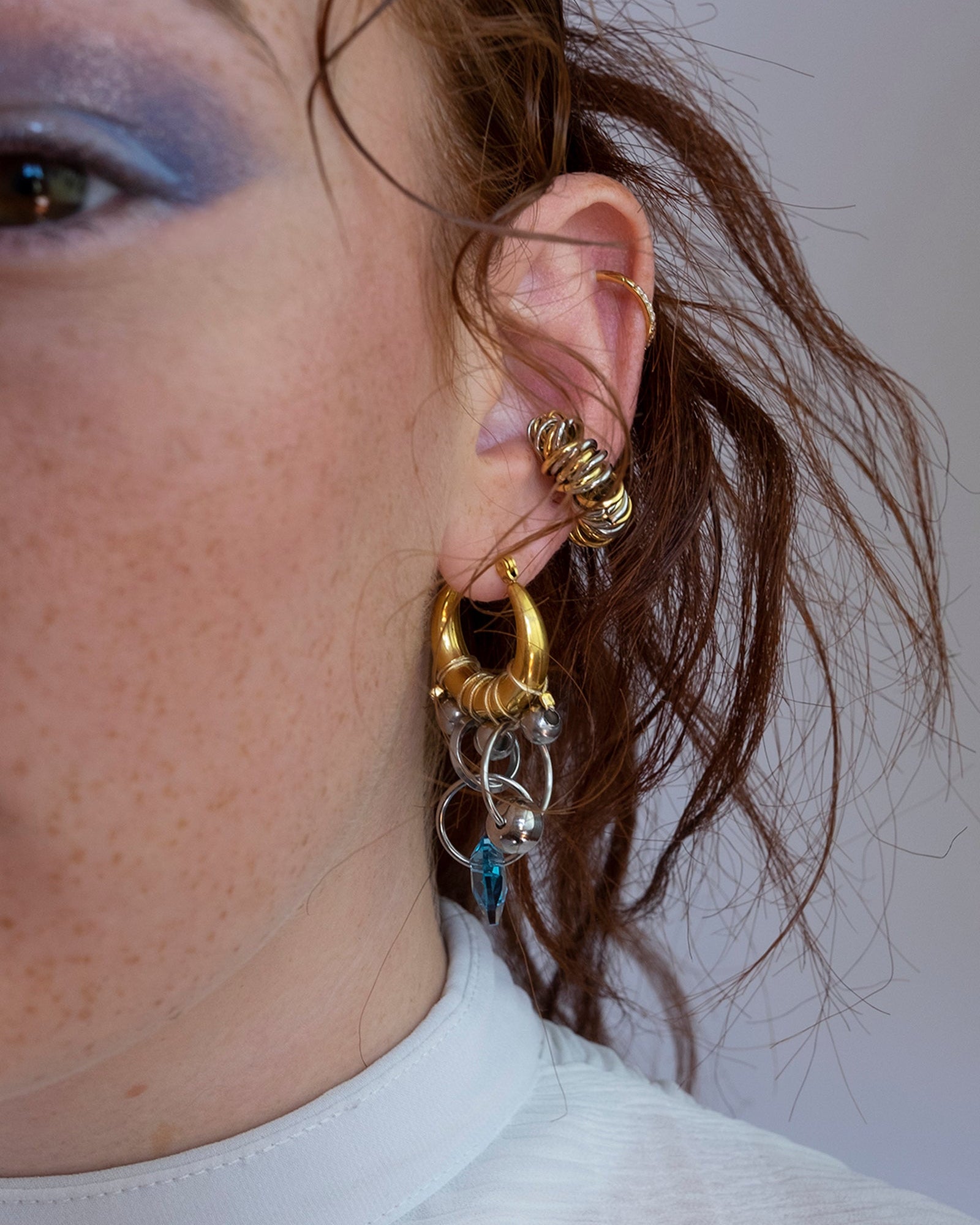 Mono boucle d’oreilles en acier inoxydable composée d’une créole doré, de différents anneaux argenté, d'une perle argenté et d'un coeur en cristal
