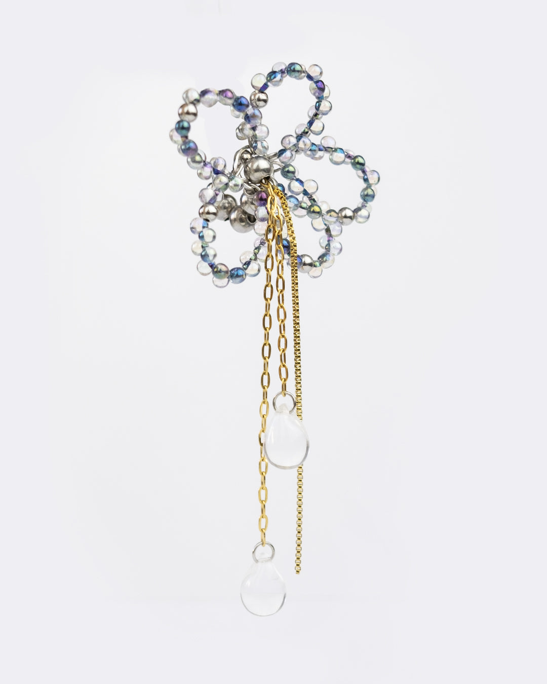 Earcuff en acier inoxydable. Il s’agit d’un faux piercing pour oreille non perçée qui se positionne au niveau du conch ou du lobe suivant la largeur de l’oreille. Il est composé d’un anneau argenté, d'une sculpture en perles en verre en forme de fleur et de chaine doré avec des perles goutte au bout