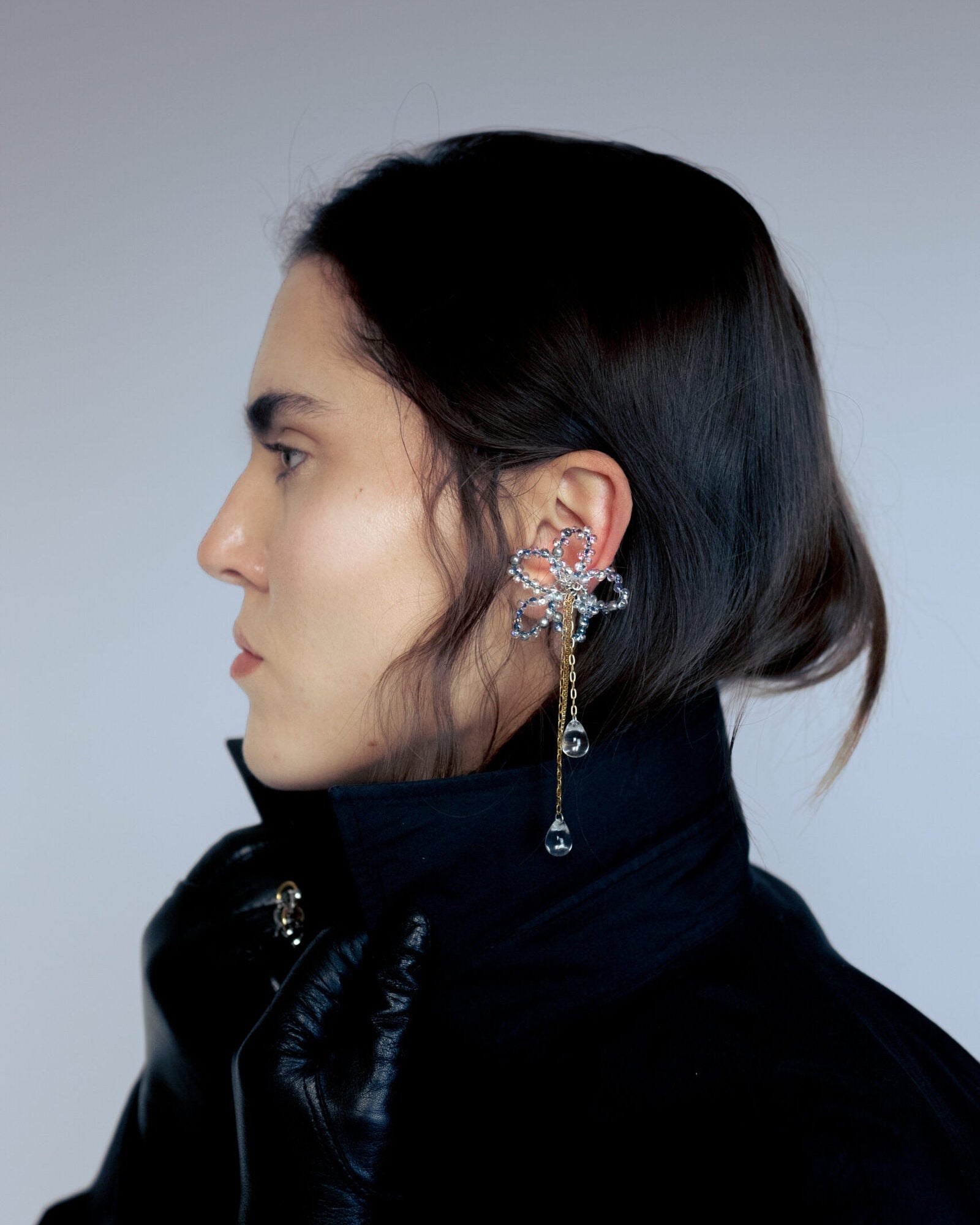 Earcuff en acier inoxydable. Il s’agit d’un faux piercing pour oreille non perçée qui se positionne au niveau du conch ou du lobe suivant la largeur de l’oreille. Il est composé d’un anneau argenté, d'une sculpture en perles en verre en forme de fleur et de chaine doré avec des perles goutte au bout