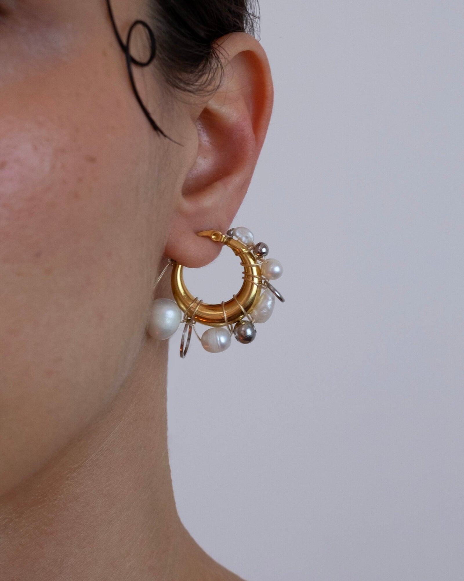 Mono boucle d’oreilles en acier inoxydable composée d’une créole dorée, de perles de culture et d'anneaux argentés de différentes tailles tressés autour de la boucle