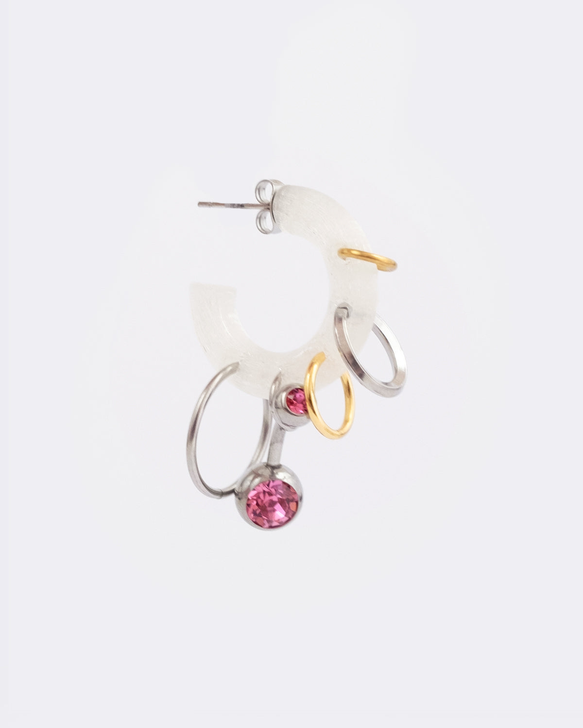 Mono boucle d’oreilles en plastique biosourcé. Elle est composée de différents anneaux dorés et argentés avec un piercing rose sur une base transparente