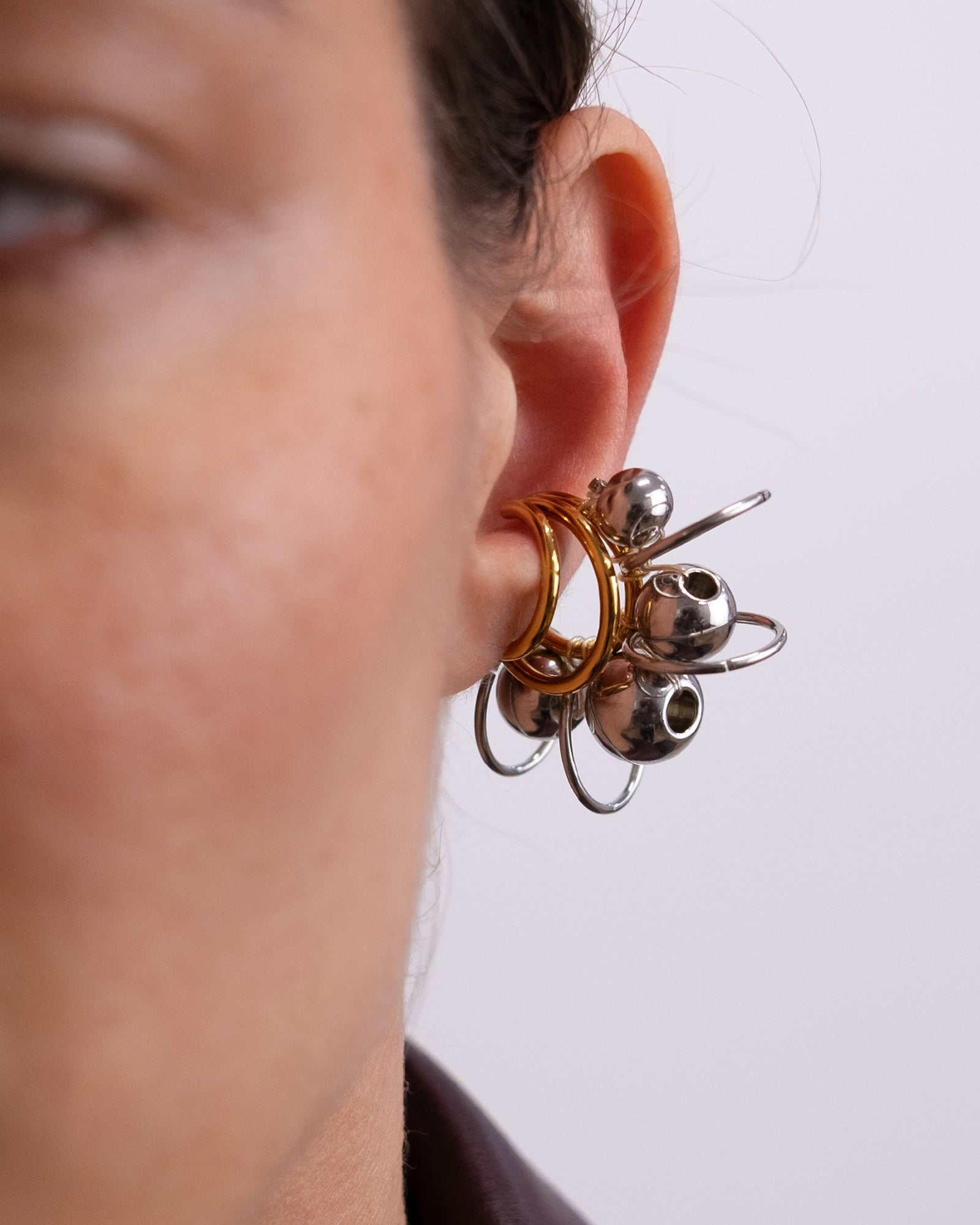 Earcuff en acier inoxydable. Il s’agit d’un faux piercing pour oreille non perçée qui se positionne au niveau du conch ou du lobe suivant la largeur de l’oreille. Il est composé d’un triple anneau doré autour duquel sont tressés des perles et anneaux argentés de différentes tailles.