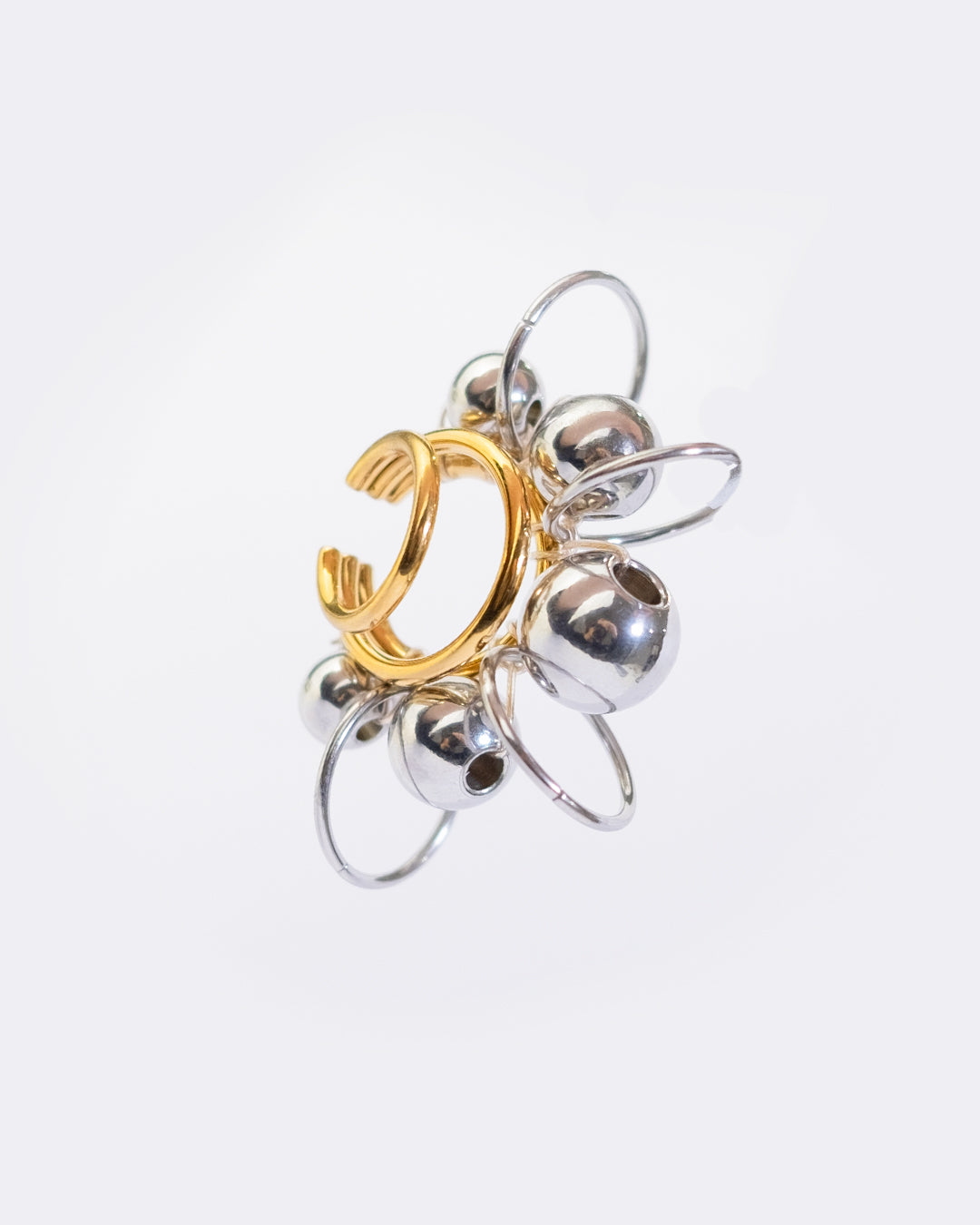 Earcuff en acier inoxydable. Il s’agit d’un faux piercing pour oreille non perçée qui se positionne au niveau du conch ou du lobe suivant la largeur de l’oreille. Il est composé d’un triple anneau doré autour duquel sont tressés des perles et anneaux argentés de différentes tailles.