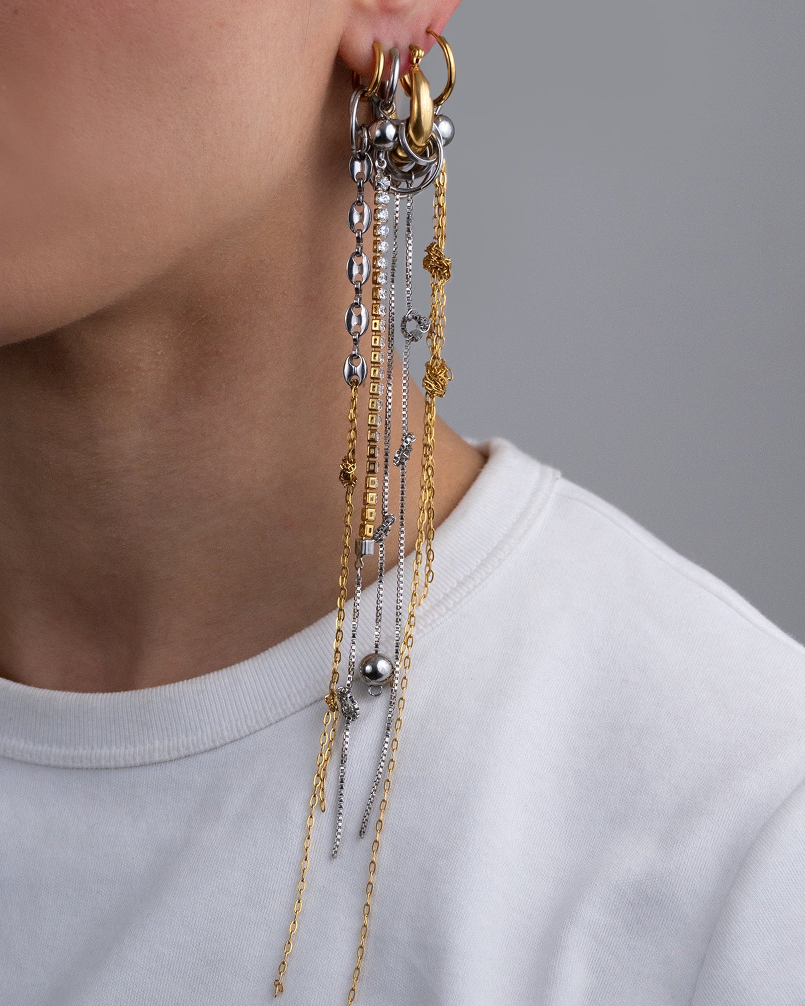 Mono boucle d’oreilles en acier inoxydable composée d’une créole dorée, d'anneaux argentés de différentes tailles, et de chaines pendantes nouées argentées.