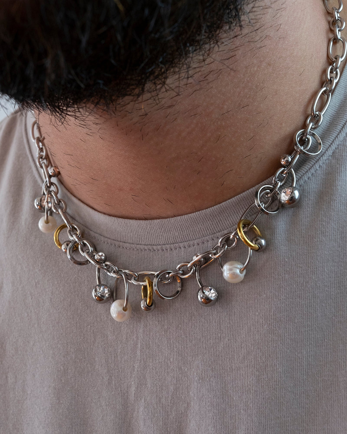 Collier en acier inoxydable porté composé d'une chaîne argentée agrémentée d'anneaux de différentes tailles de perles de culture d'eau douce ainsi que de piercings