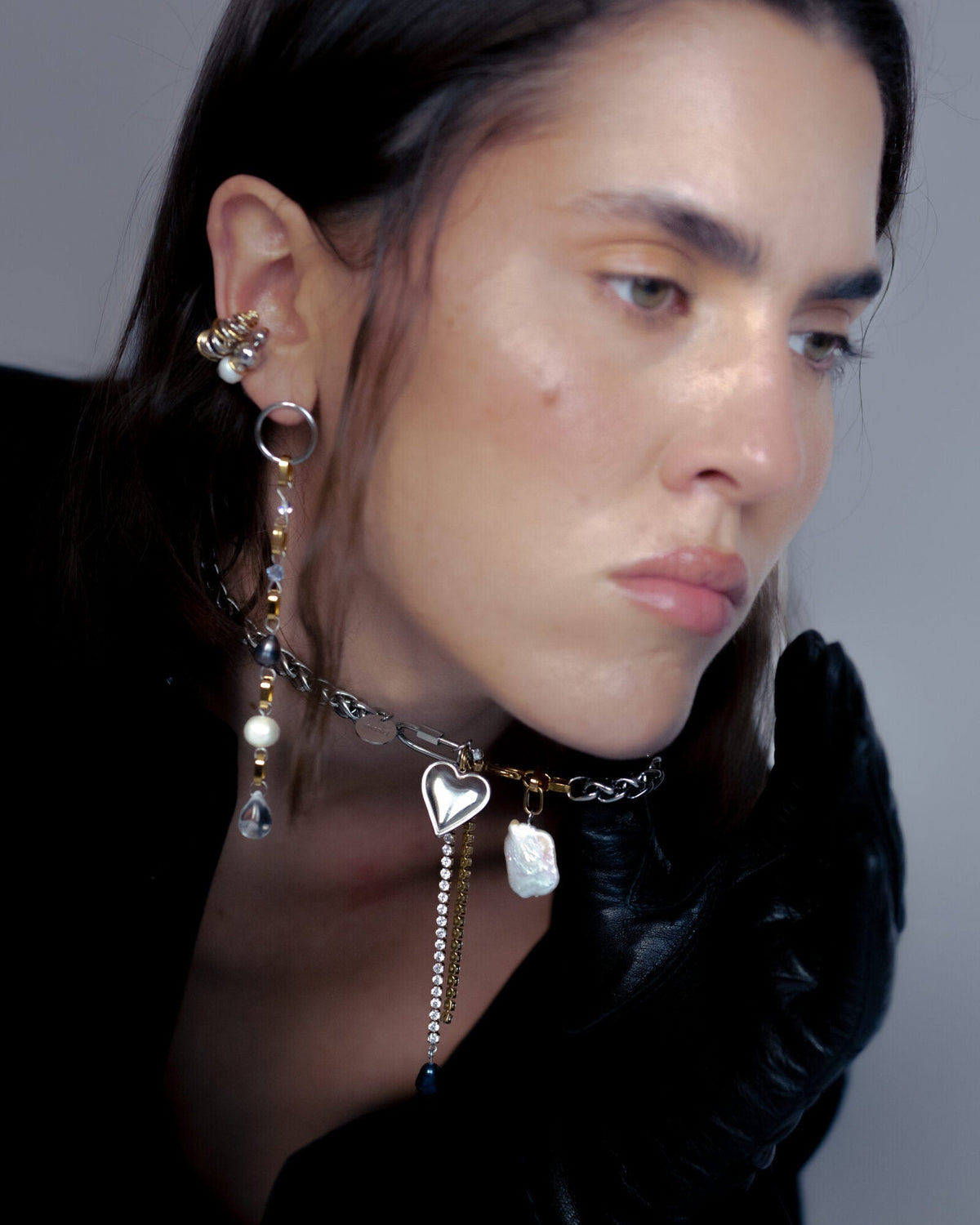 Collier en acier inoxydable porté composé d'une chaîne argentée avec deux mousquetons contenant un pendentif cœur argenté et deux chaînes en strass avec une perle de culture d'eau douce noire sur l'une d'elles