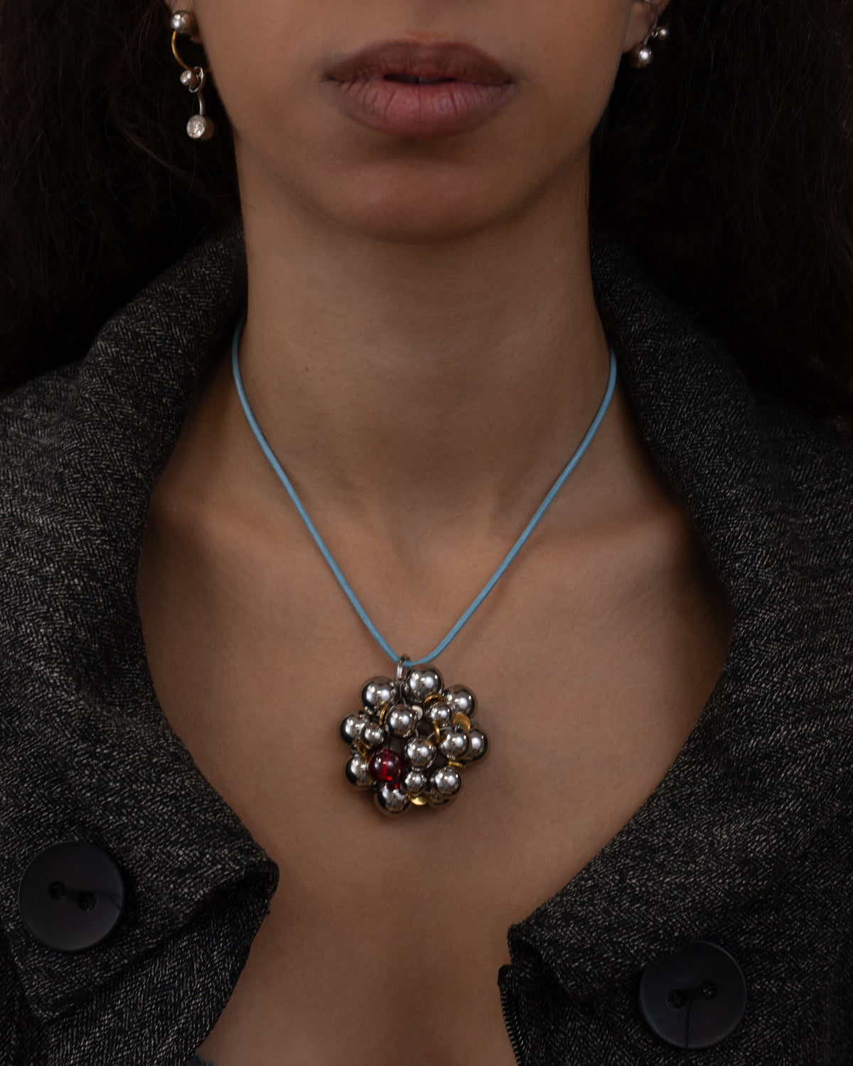 Collier en acier inoxydable porté composé d'un cordon en cuir bleu avec un pendentif sphérique en perles argentées grains de café dorés et perle en verre rouge