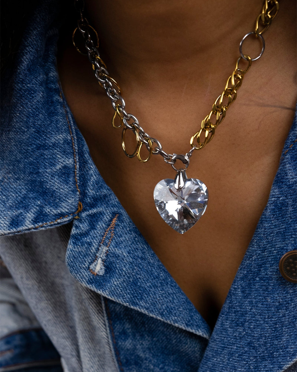 Collier en acier inoxydable porté composé d'une chaîne dorée et argentée entrelacée de plusieurs anneaux, avec un pendentif cœur en cristal