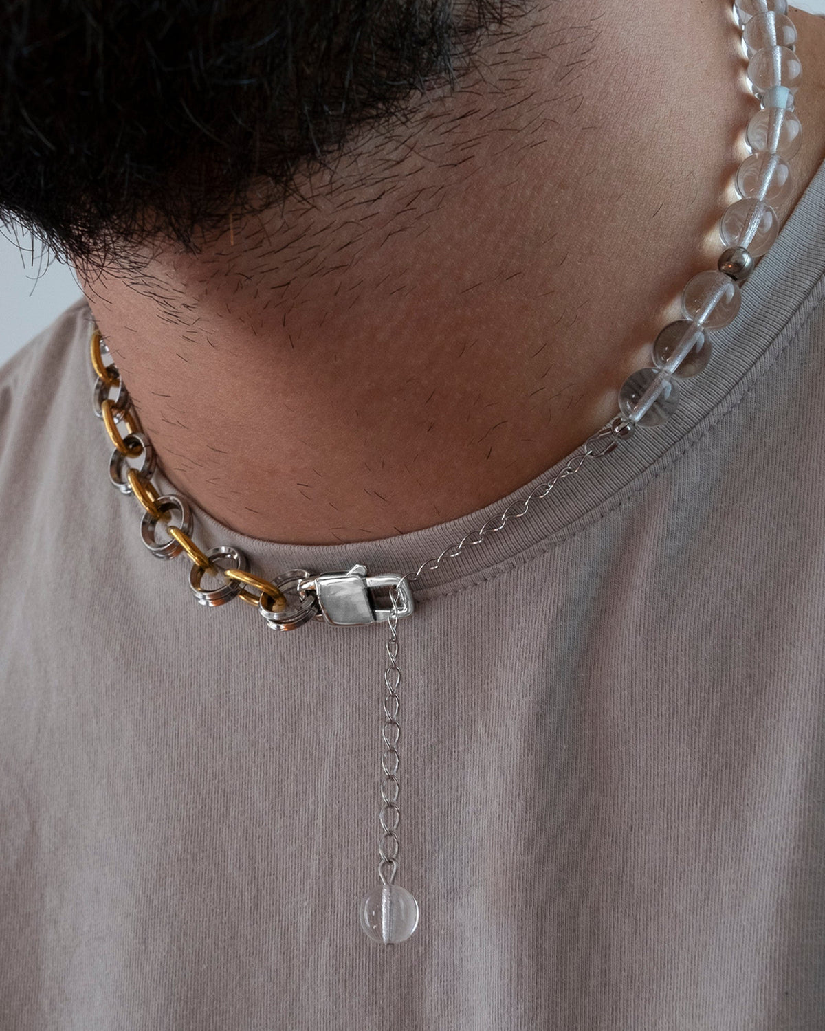 Collier en acier inoxydable porté au cou modulable en deux bracelets l'un est composé d'anneaux dorés et argentés et l'autre de perles en verre