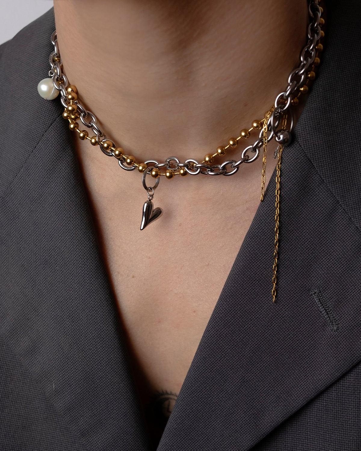 Collier en acier inoxydable porté composé d'une chaîne bille dorée et d'une chaîne argentée entremêlée agrémentées d'un pendentif cœur et d'une perle de culture d'eau douce