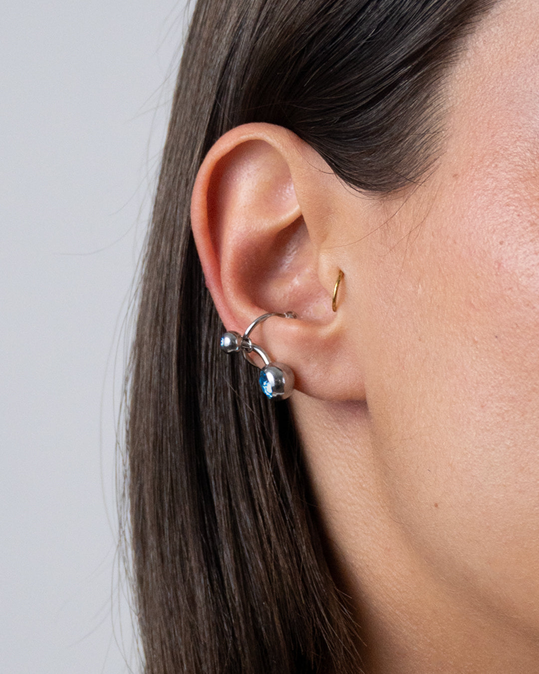 Earcuff en acier inoxydable qui se positionne au niveau du conch ou du lobe suivant la largeur de l’oreille porté composé d’un anneau argenté et d’un piercing avec un zirconium cristal bleu