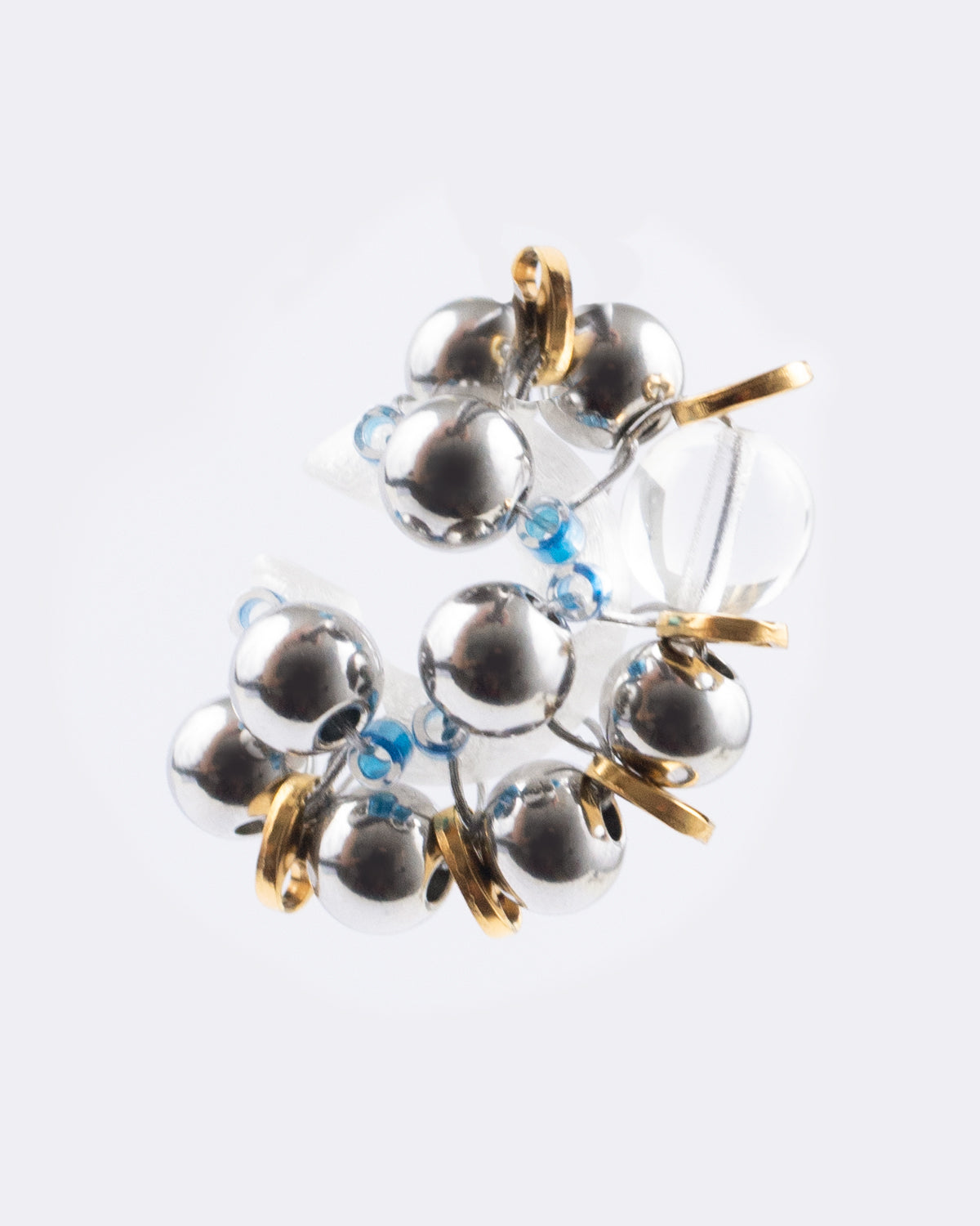Earcuff Jelly Duo Bleu porté en plastique biosourcé composé d'une multitude de perles argentées de grains de café dorés et de perles en verre colorées bleues tressés sur une base transparente