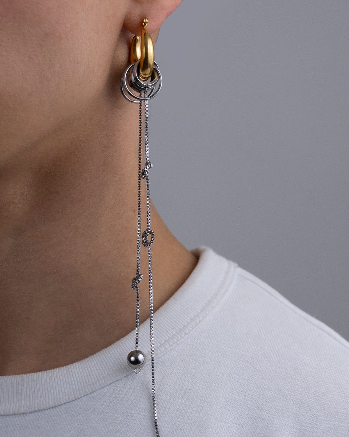 Mono boucle d’oreilles en acier inoxydable porté composée d’une créole dorée d’anneaux argentés de différentes tailles et de chaînes pendantes nouées argentées