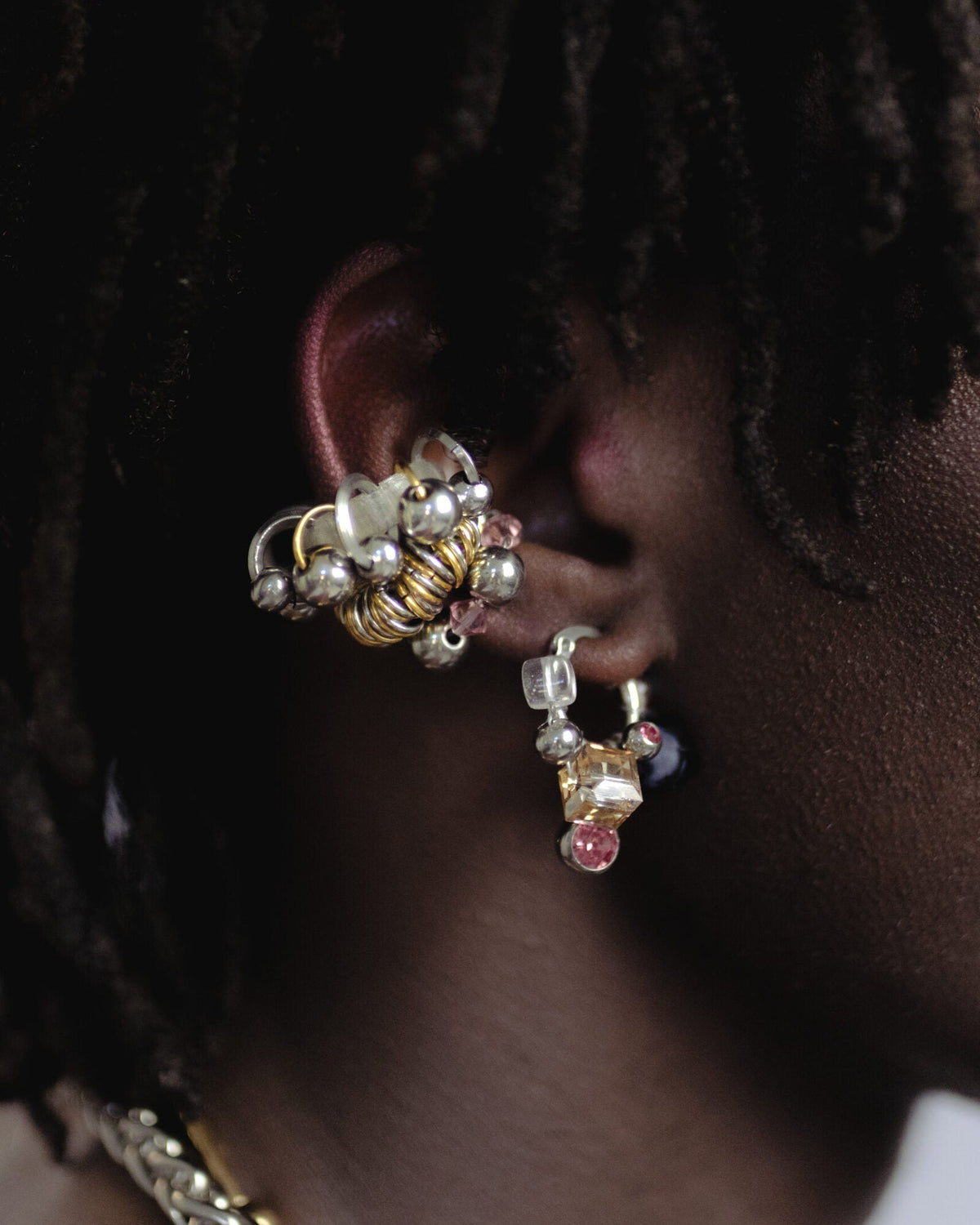 Mono boucle d’oreilles en acier inoxydable porté composée d’une créole argentée de perles en cristal en verre et synthétiques ainsi que d’un piercing tressés autour de la boucle