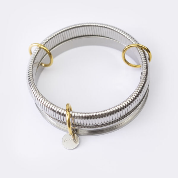 Bracelet en acier inoxydable. Il s'agit de deux joncs argenté liés par des anneaux doré, dont un contient un médaillon de la marque poinçonné à la main