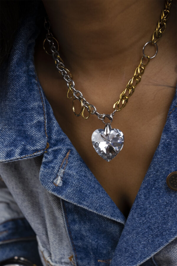 Il s'agit d'un collier composé d'une chaine doré et argenté entrelaissés de plusieurs anneaux, avec un pendentif coeur en cristal
