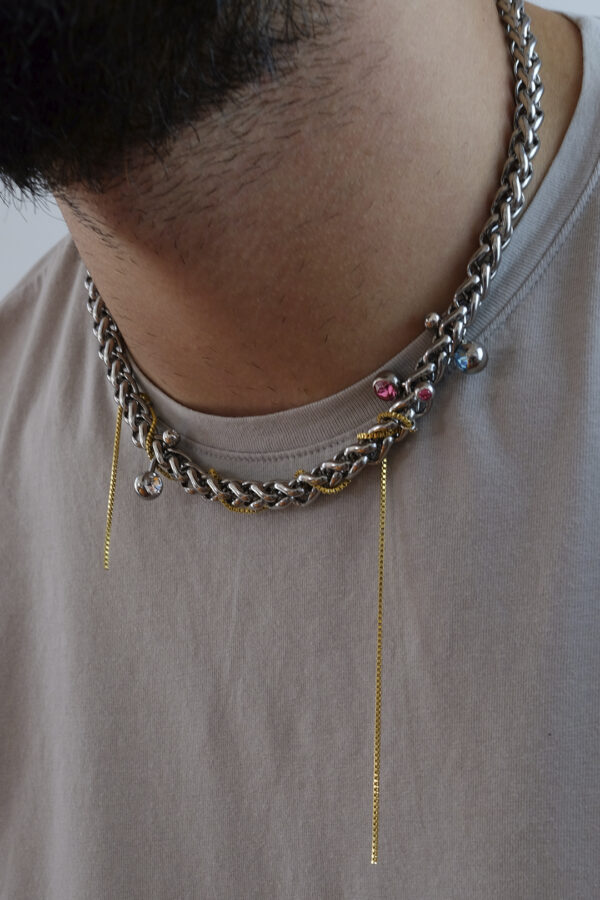 Collier en acier inoxydable. Il s'agit d'un collier composé d'une chaine argenté, d'une chaine doré entremêlée et de piercing de couleur différentes