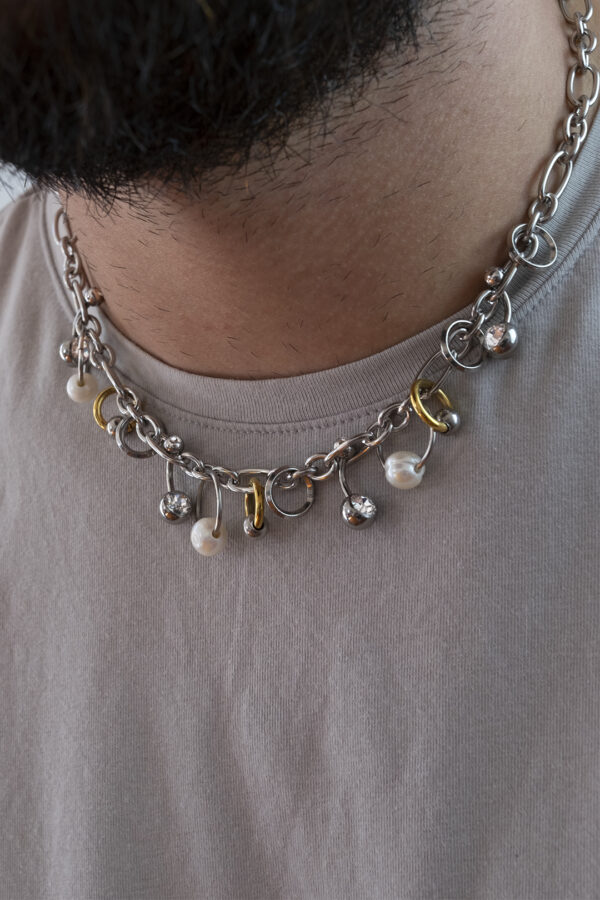 Collier en acier inoxydable. Il s'agit d'un collier composé d'une chaine argenté agrémenté d'anneaux de différentes tailles, de perles de culture d'eau douce ainsi que de piercing