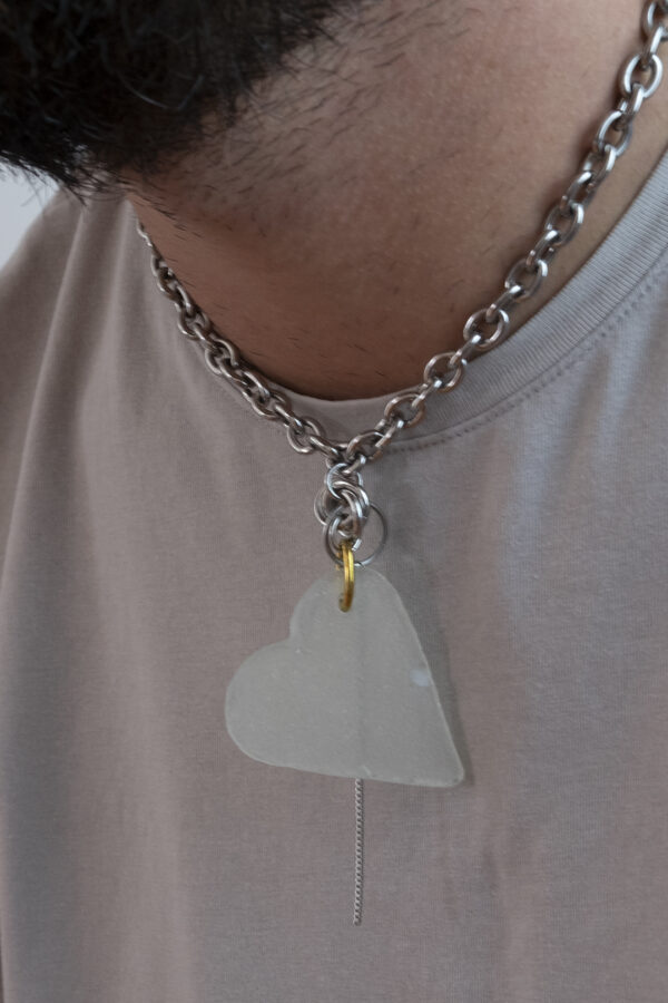 Collier en acier inoxydable. Il s'agit d'un collier ras de cou composé d'une chaine argenté et d'un morceau de verre poli ramassé sur la plage et façonné en forme de coeur.