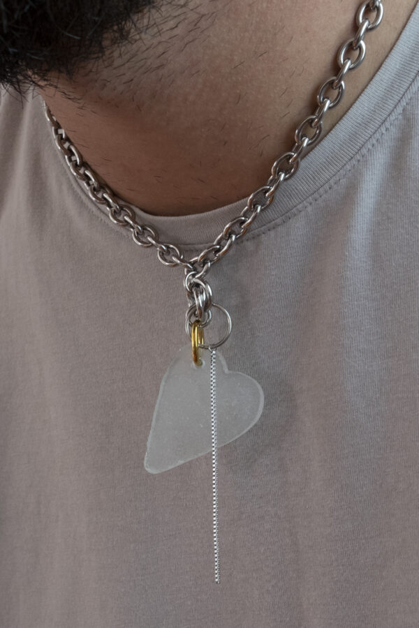 Collier en acier inoxydable. Il s'agit d'un collier ras de cou composé d'une chaine argenté et d'un morceau de verre poli ramassé sur la plage et façonné en forme de coeur.