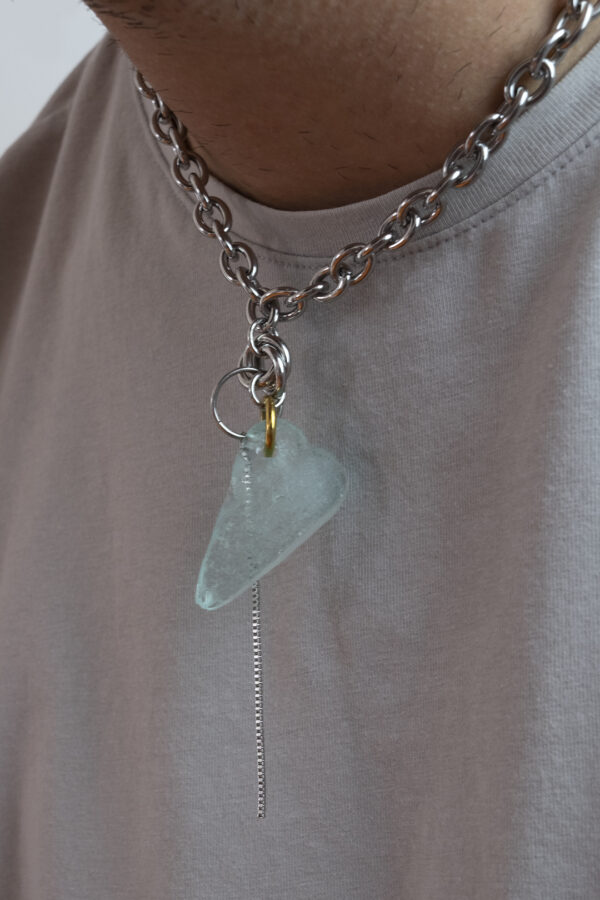 Collier en acier inoxydable. Il s'agit d'un collier ras de cou composé d'une chaine argenté et d'un morceau de verre poli ramassé sur la plage et façonné en forme de coeur.